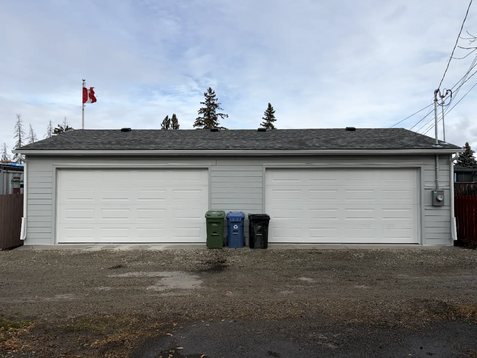 After: a new detached double garage with two white overhead doors and grey siding, built by Alliance Renovations