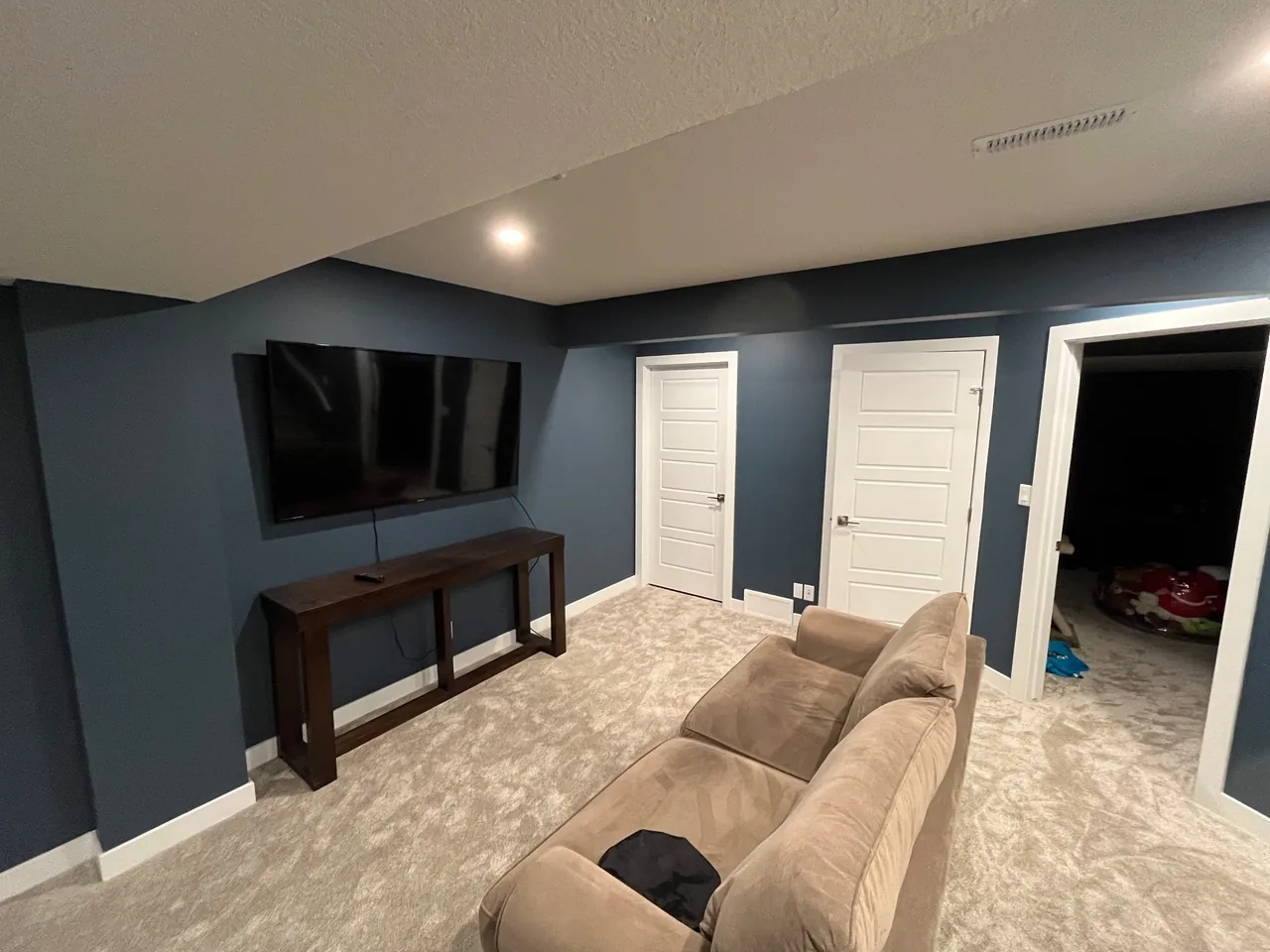 A basement media room with navy walls, carpet and a wall-mounted TV, by Alliance Renovations