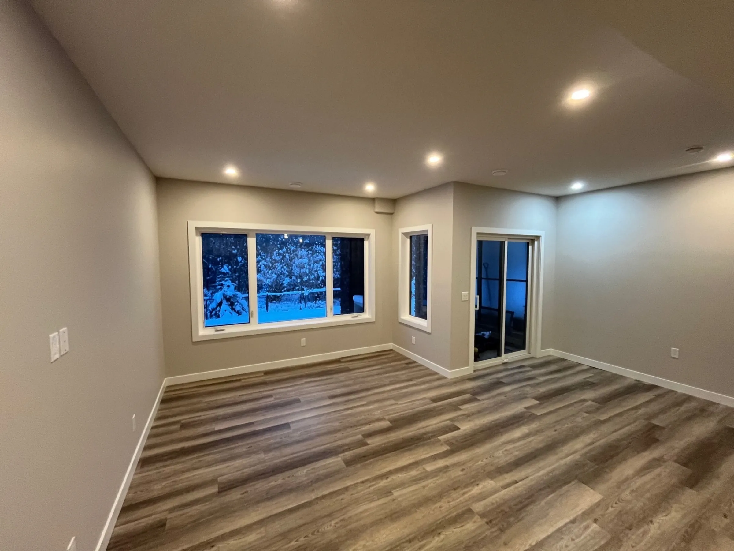 A walkout basement living room with big windows, a patio door and pot lights