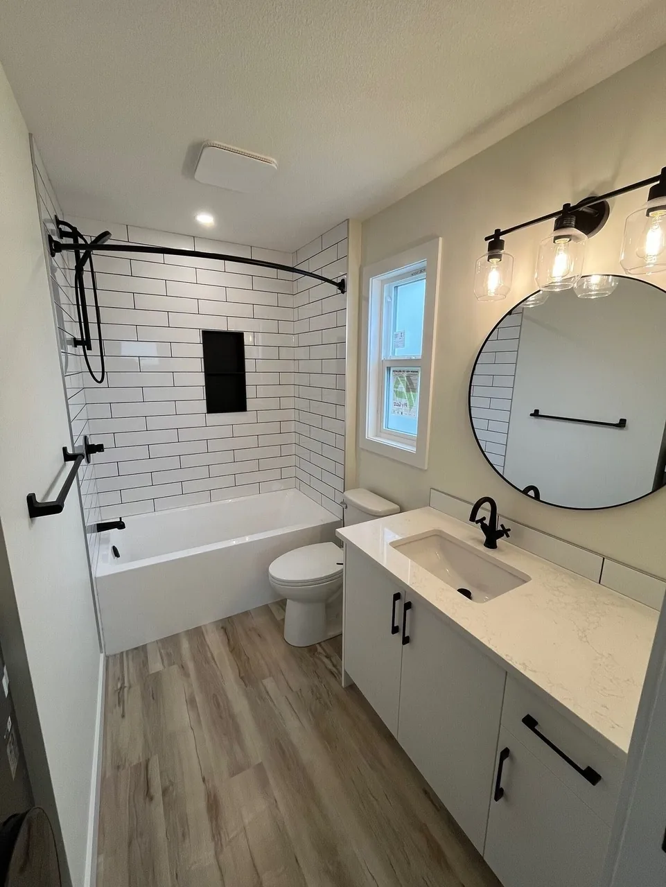 A bathroom with white subway tile, black fixtures and a round mirror