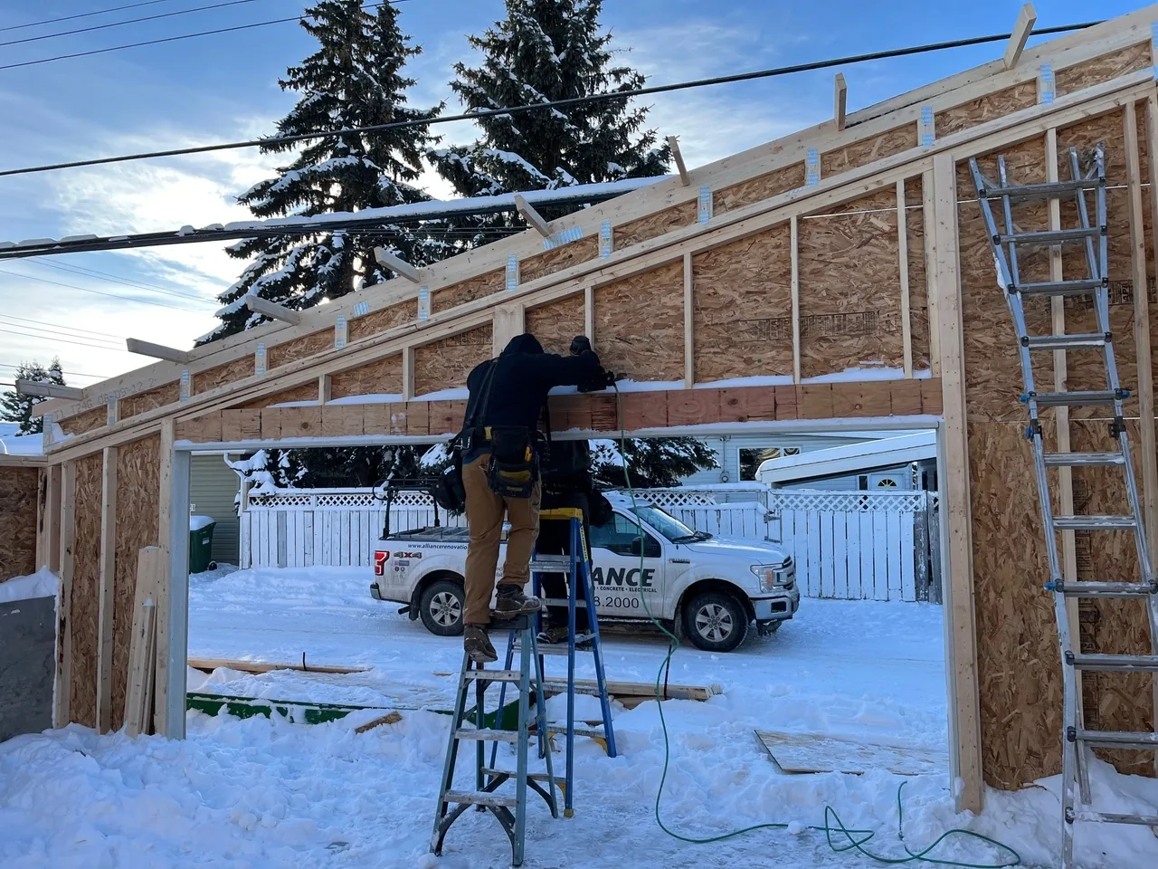 An Alliance crew framing a garage in the snow, with the company truck behind