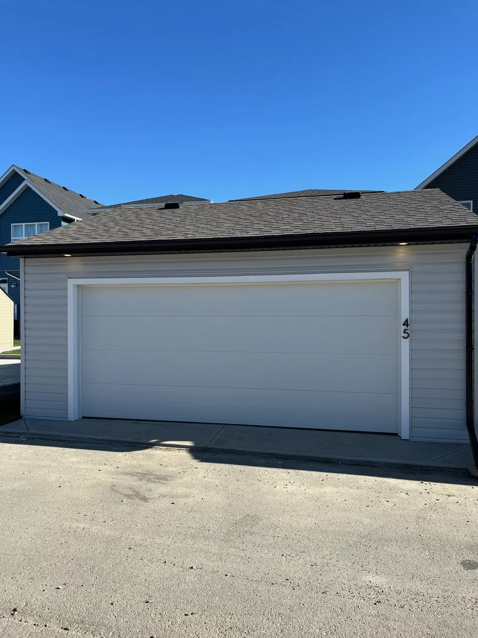 A light grey garage with a flush white door and soffit lights, built by Alliance