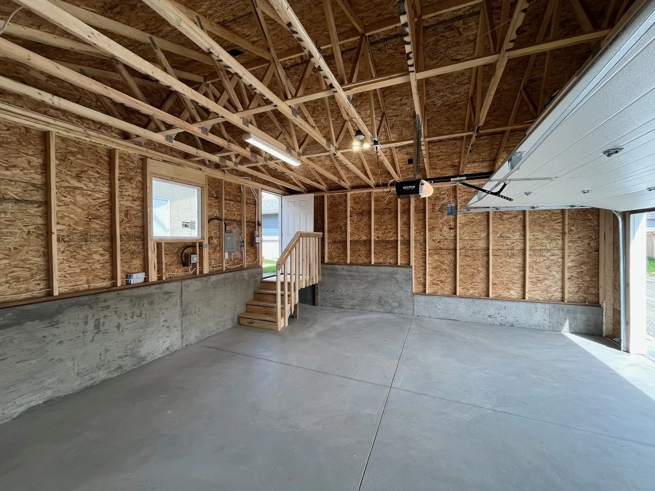 An open-framed garage interior with concrete stem walls and wood stairs up to the man door