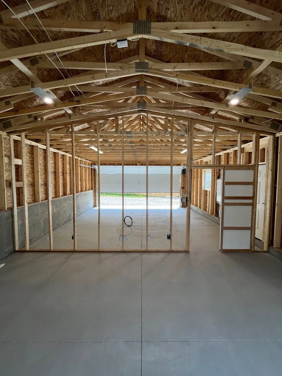 Interior walls going in inside a new garage build, with trusses and lights overhead