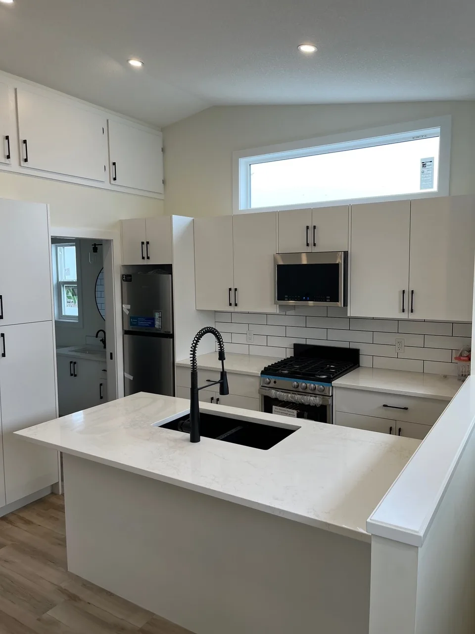 A white suite kitchen with a quartz peninsula, black sink and gas range